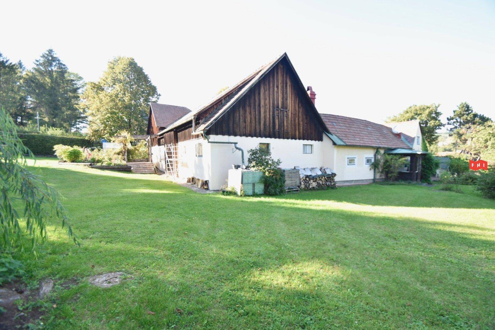 Rückansicht des Landhauses mit großem Garten und Holzfassade unter blauem Himmel.