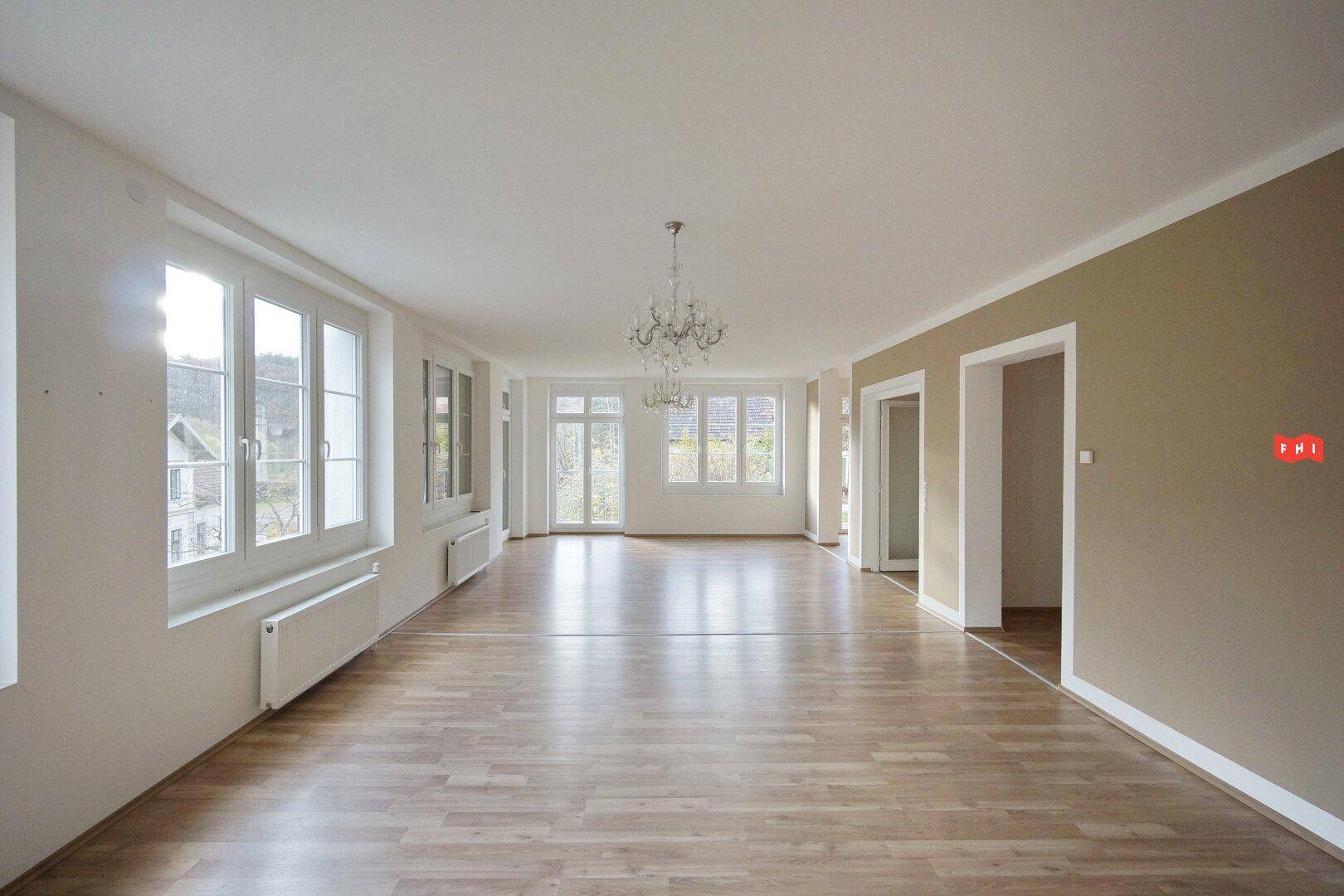 Geräumiges, helles Wohnzimmer mit Parkettboden, großen Fenstern und Kronleuchter.