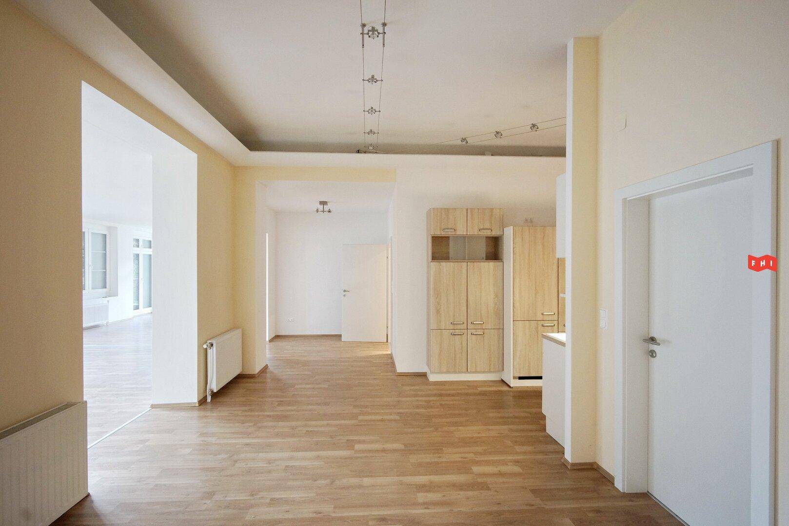 Heller offener Bereich mit Holzboden und Einbauküche in hellem Holzton.