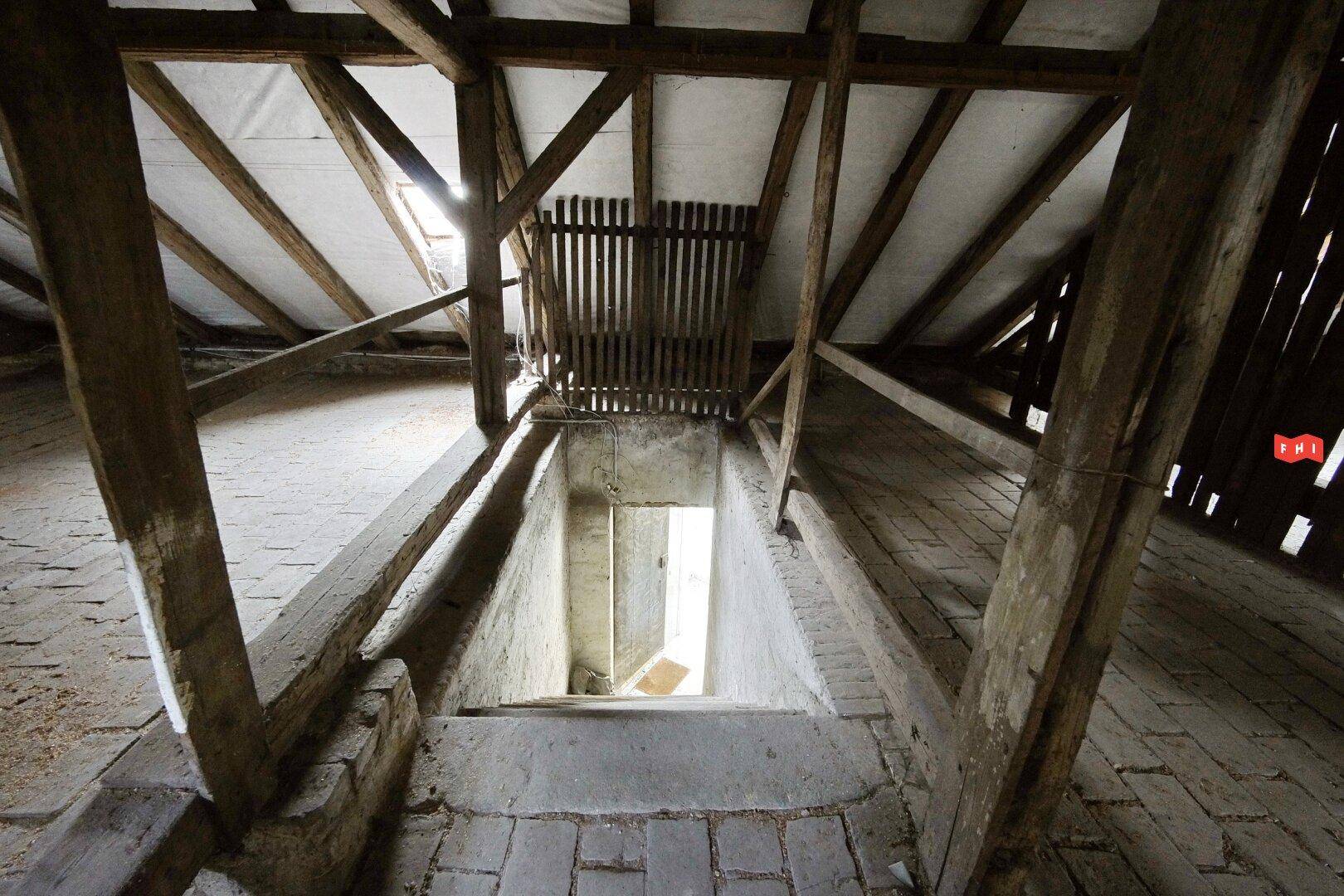 Blick vom Dachboden in ein Treppenhaus, umgeben von der robusten Holzkonstruktion des Daches.