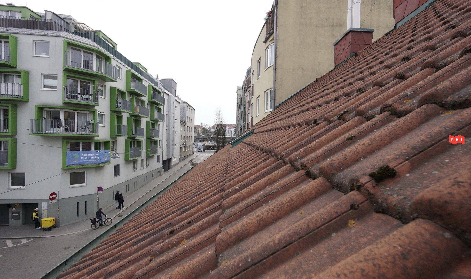 Dachansicht mit roten Ziegeln und Blick auf eine belebte Straße mit modernen Gebäuden im Hintergrund.