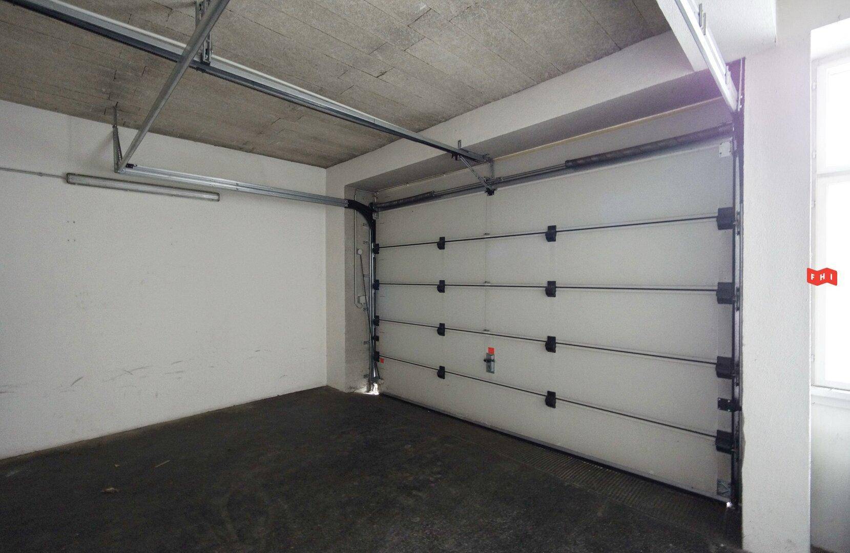 Innenansicht der Garage mit robustem Garagentor, Betonboden und funktionaler Deckenbeleuchtung.