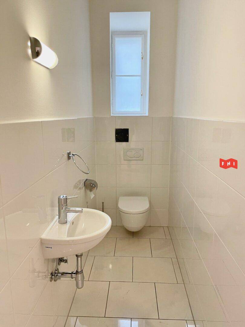 Separates Gäste-WC mit kleinem Waschbecken, Wand-WC und Fenster.