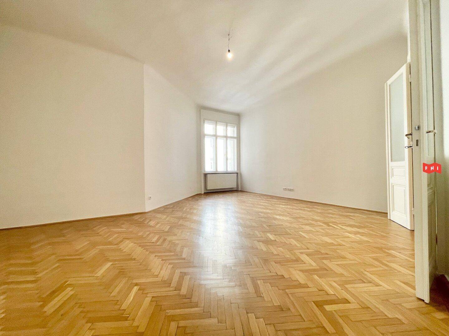 Heller Raum mit Fischgrätparkett und großem Fenster, ideal als Wohn- oder Schlafzimmer.