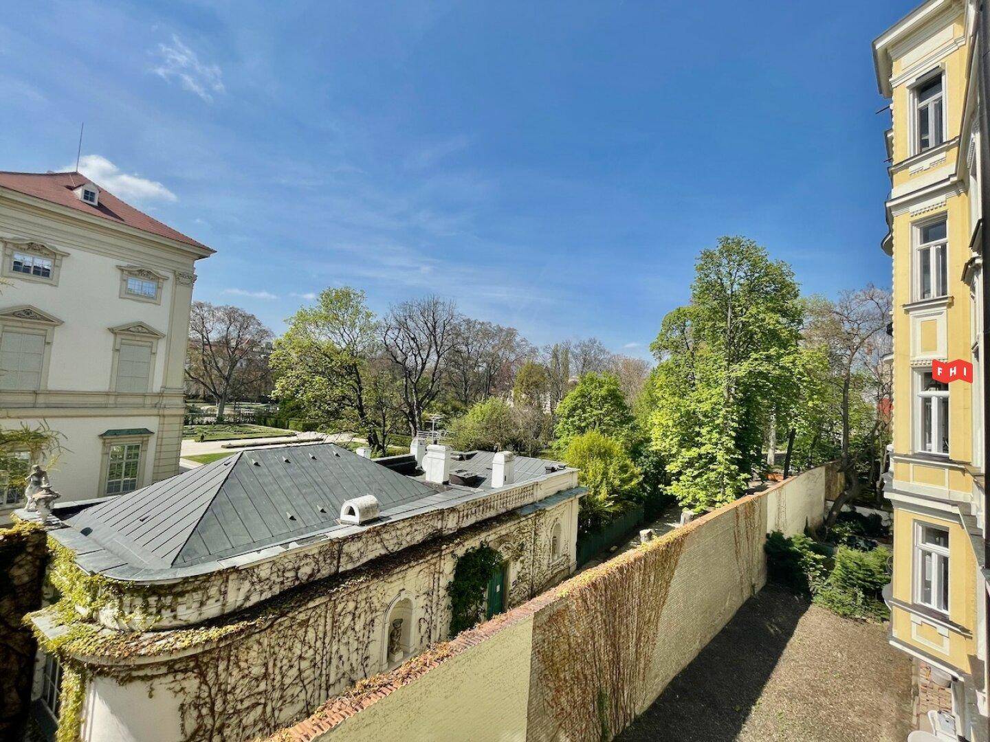 Panoramablick auf eine grüne Gartenanlage und ein historisches Gebäude unter blauem Himmel.