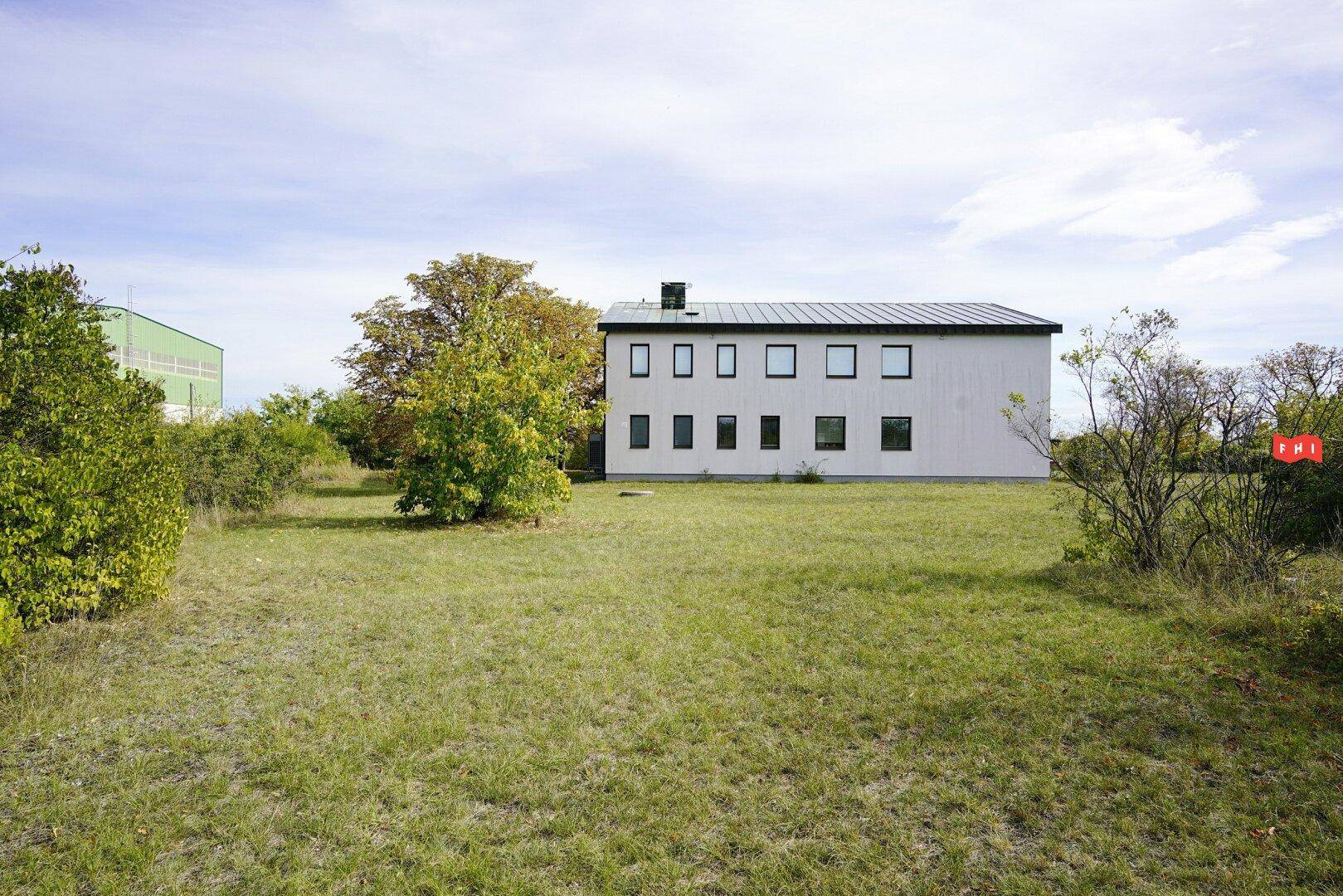 Weitläufige Grünfläche vor einem modernen Gebäude mit vielen Fenstern unter blauem Himmel.