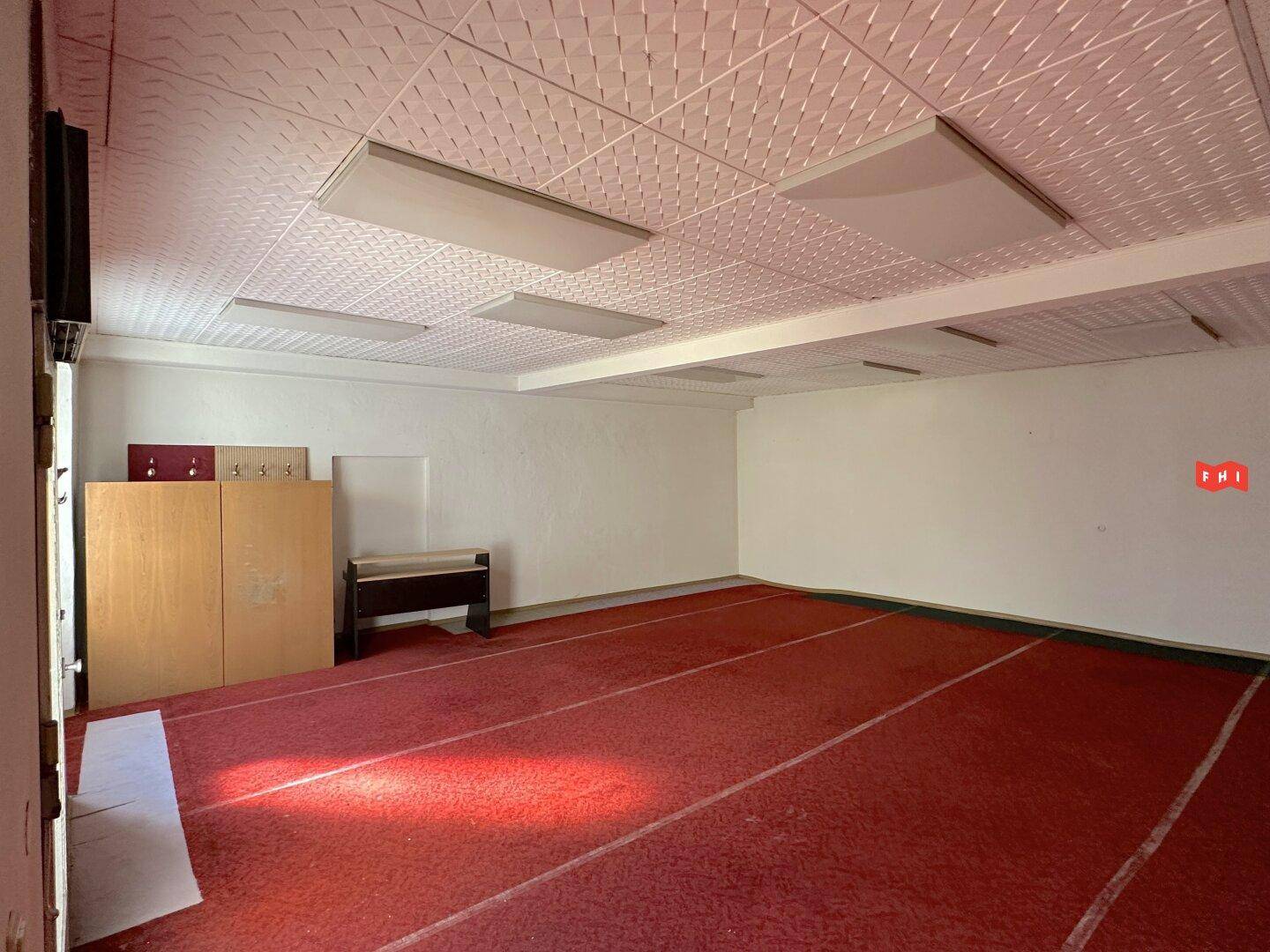 Großer Raum mit rotem Teppichboden, Deckenleuchten und einer Garderobe an der Wand.
