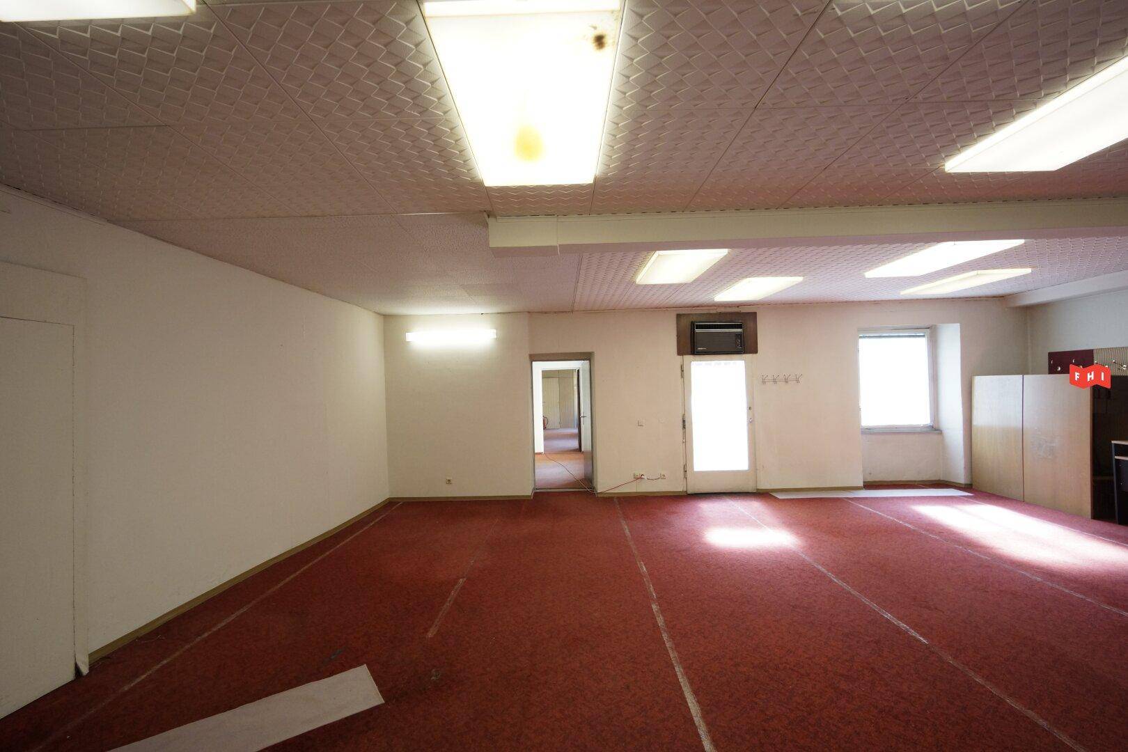 Geräumiger Innenraum mit rotem Teppichboden, Deckenbeleuchtung und Tageslicht durch Fenster.
