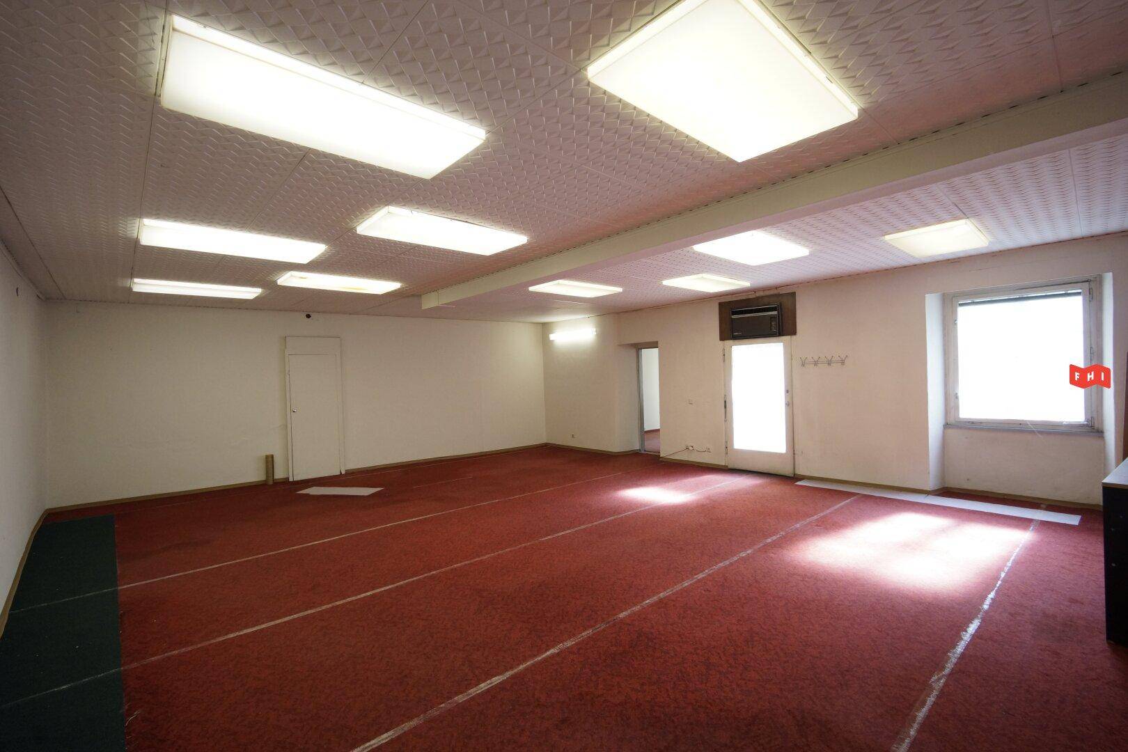 Großer leerer Raum mit rotem Teppichboden, vielen Deckenleuchten und einem Fenster.