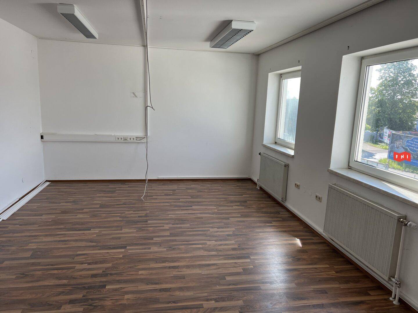 Leerer Raum mit Laminatboden, weißen Wänden und zwei Fenstern, ideal als Büro oder Arbeitszimmer.