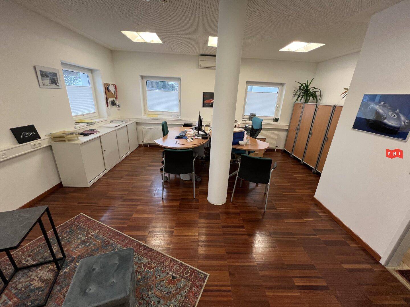 Helles Büro mit Holzparkettboden, mehreren Arbeitsplätzen und Schränken.