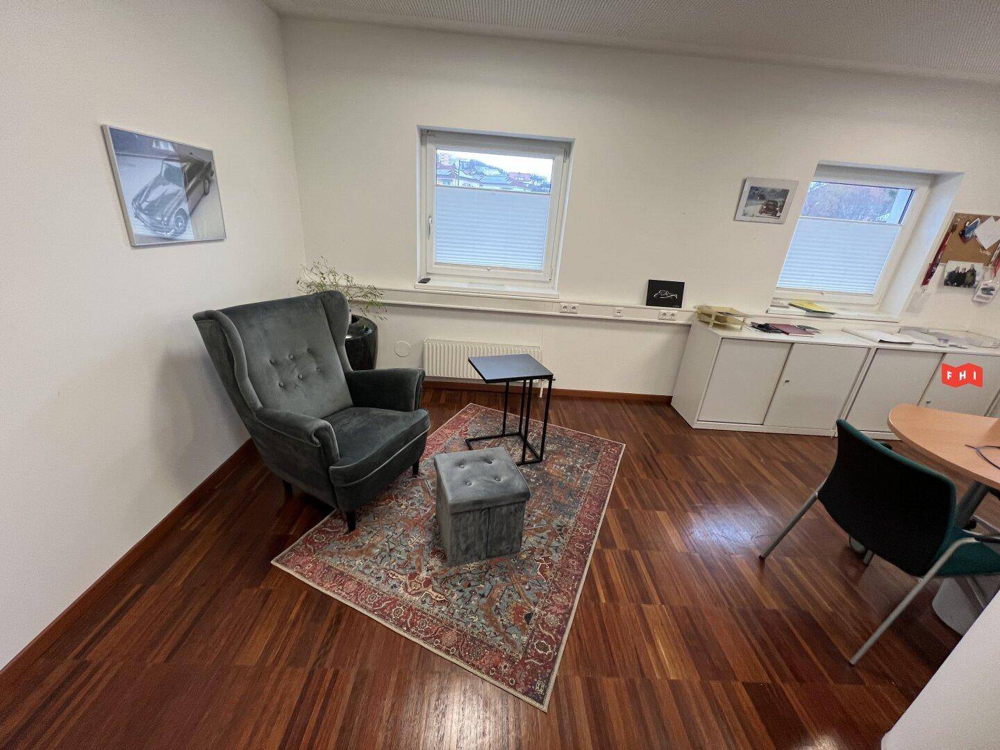 Gemütliche Sitzecke in einem Büro mit Sessel, Teppich und Holzparkettboden.