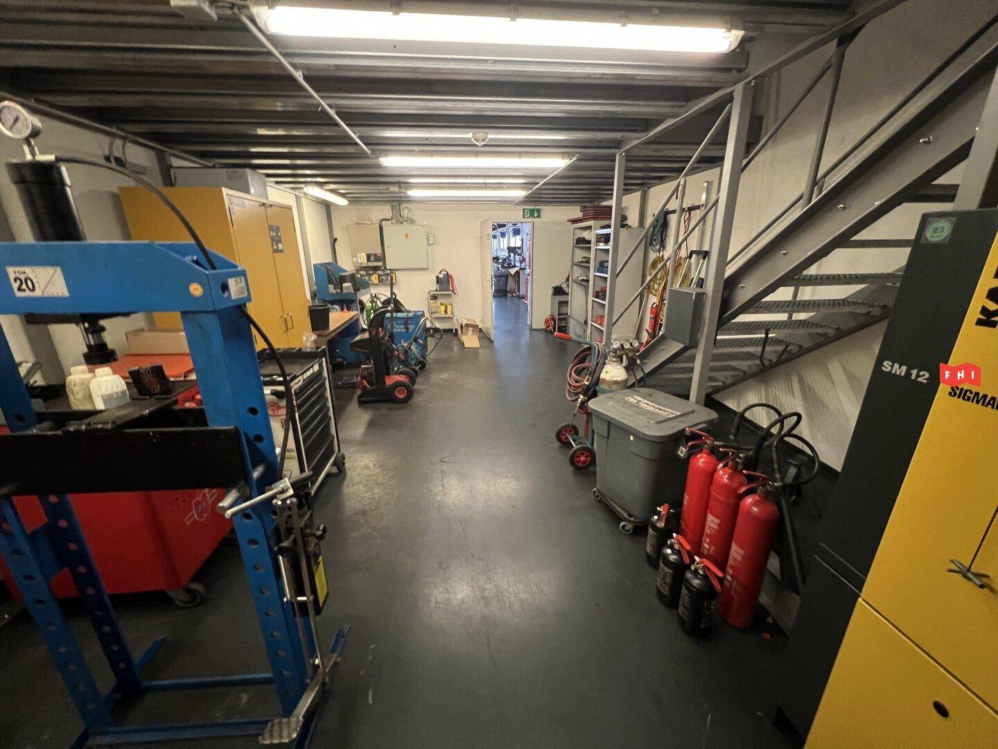 Lagerraum oder Werkstattbereich mit Regalen, Werkzeugen und einer Metalltreppe.