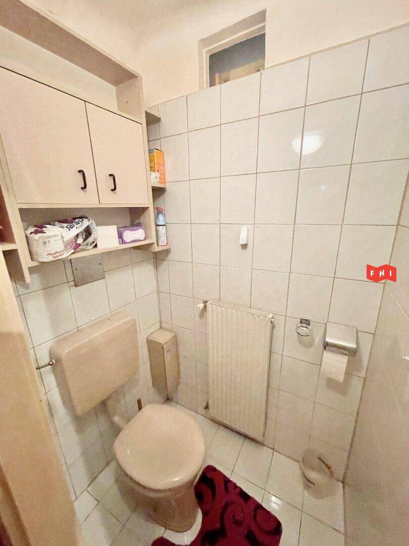 Separates WC mit Toilette, kleinem Waschbecken und Fenster für natürliche Belüftung.