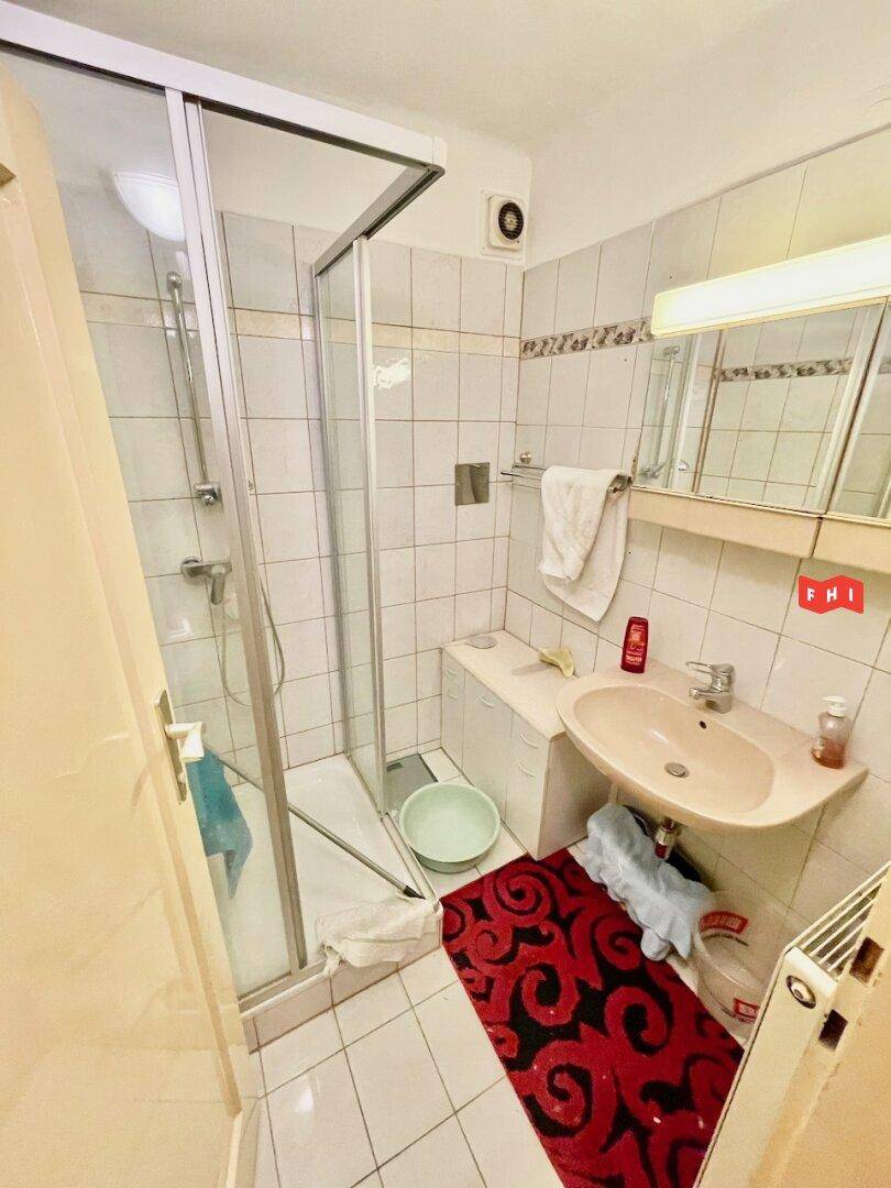 Kleines Badezimmer mit Duschkabine, Waschbecken und hellen Fliesen an den Wänden.