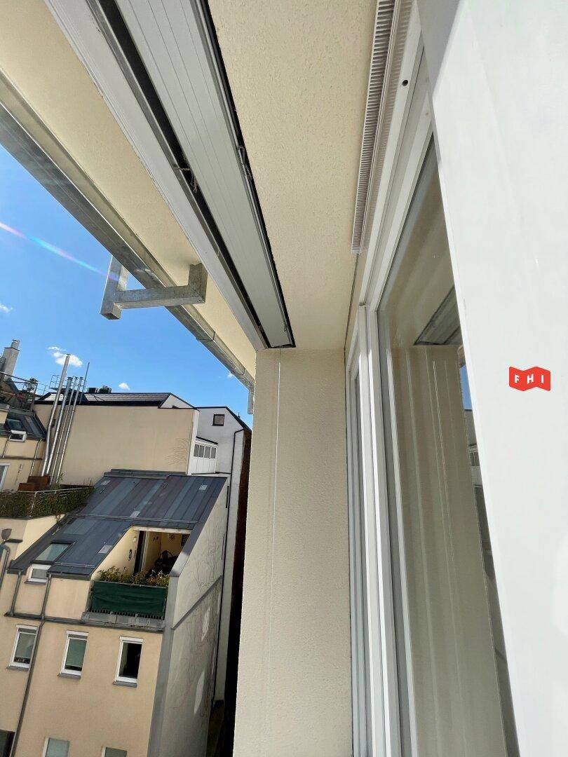 Detailansicht eines Fensters und der Außenwand mit Blick auf die Dächer der Stadt.