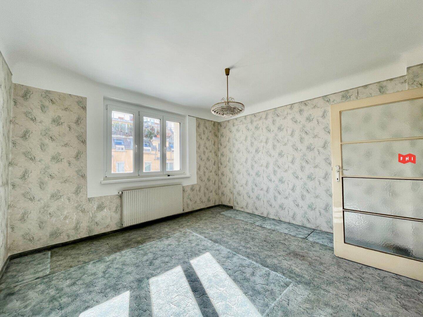 Helles Zimmer mit gemusterter Tapete, Teppichboden und einer Tür mit Milchglas.