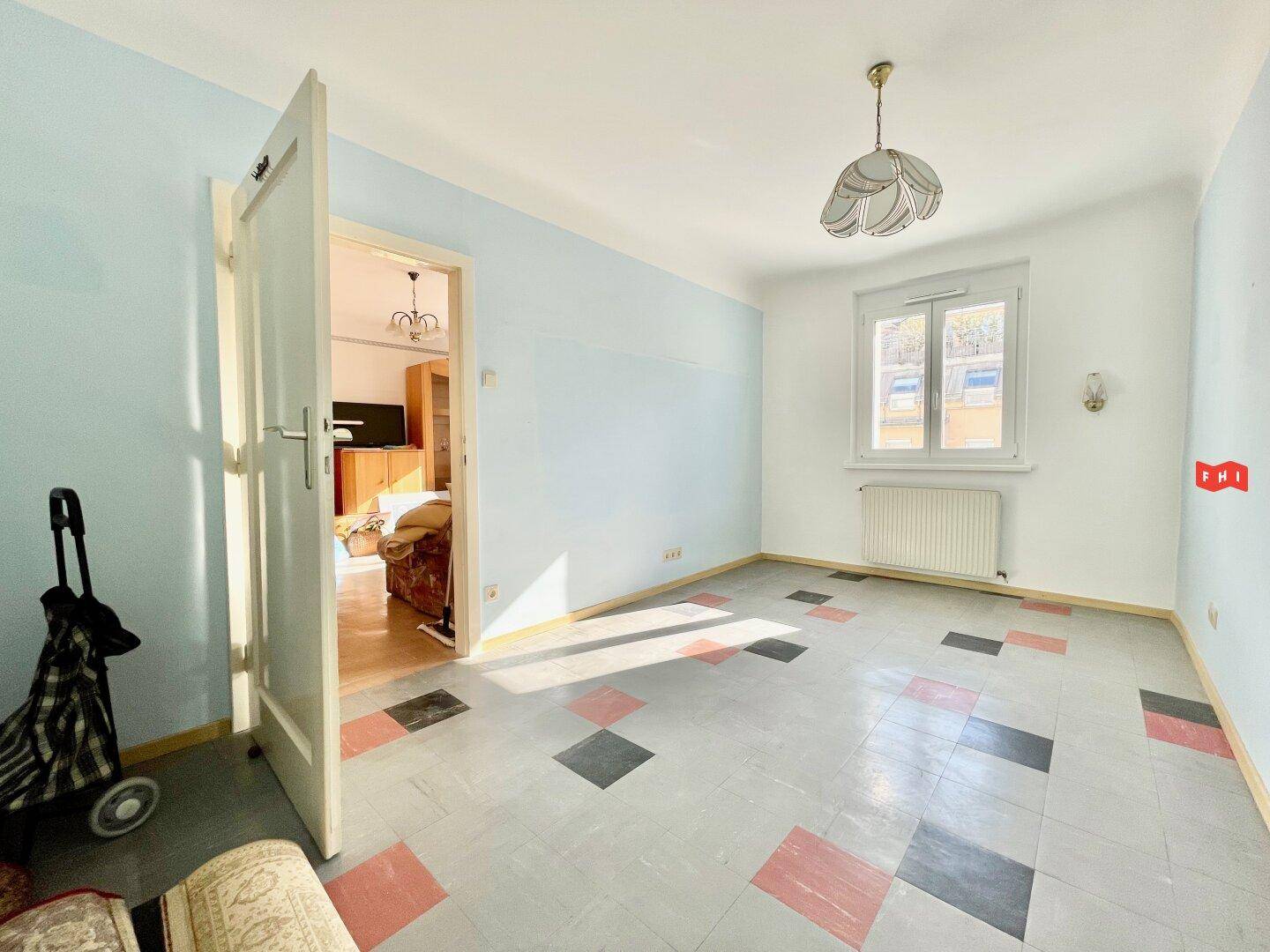 Leeres Zimmer mit blauen Wänden und einem auffälligen Fliesenboden, verbunden mit einem weiteren Raum.