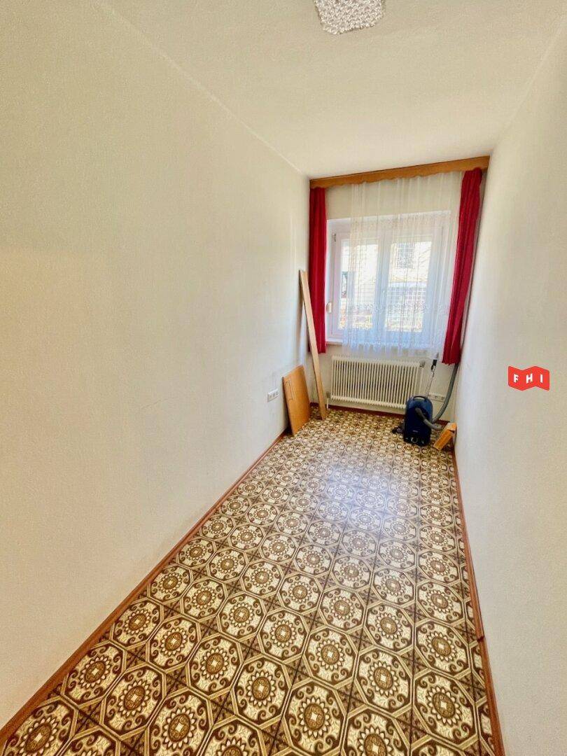 Kleiner Raum mit gemustertem Boden, Fenster und rotem Vorhang.
