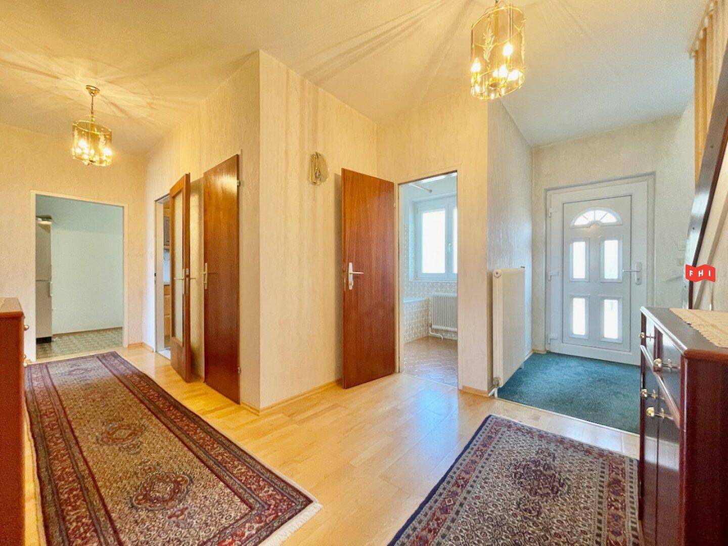 Heller Eingangsbereich mit Holzfußboden, Teppichen und Zugang zu verschiedenen Zimmern.