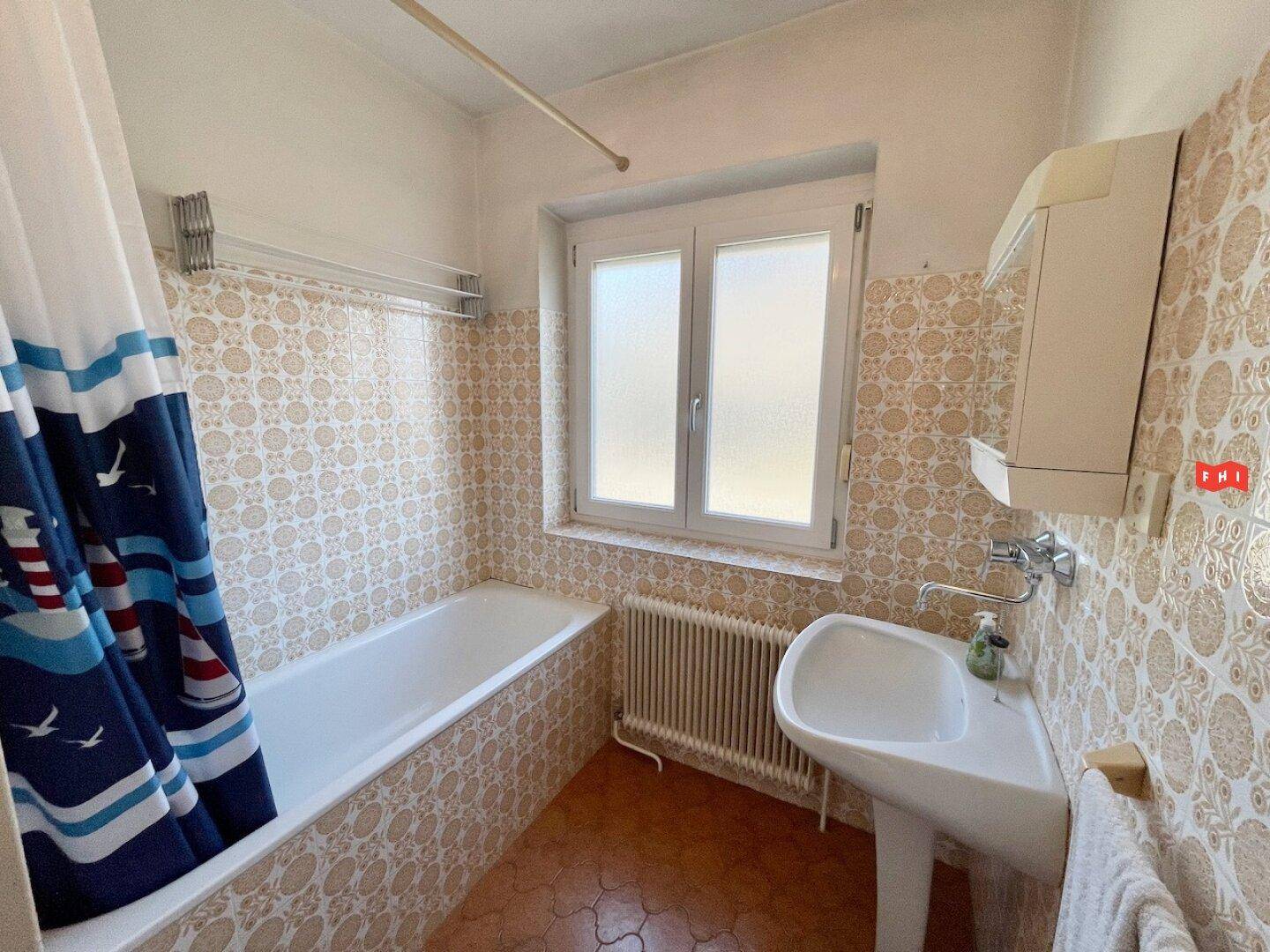 Badezimmer mit Badewanne, Waschbecken und gemusterten Fliesen im Vintage-Stil.