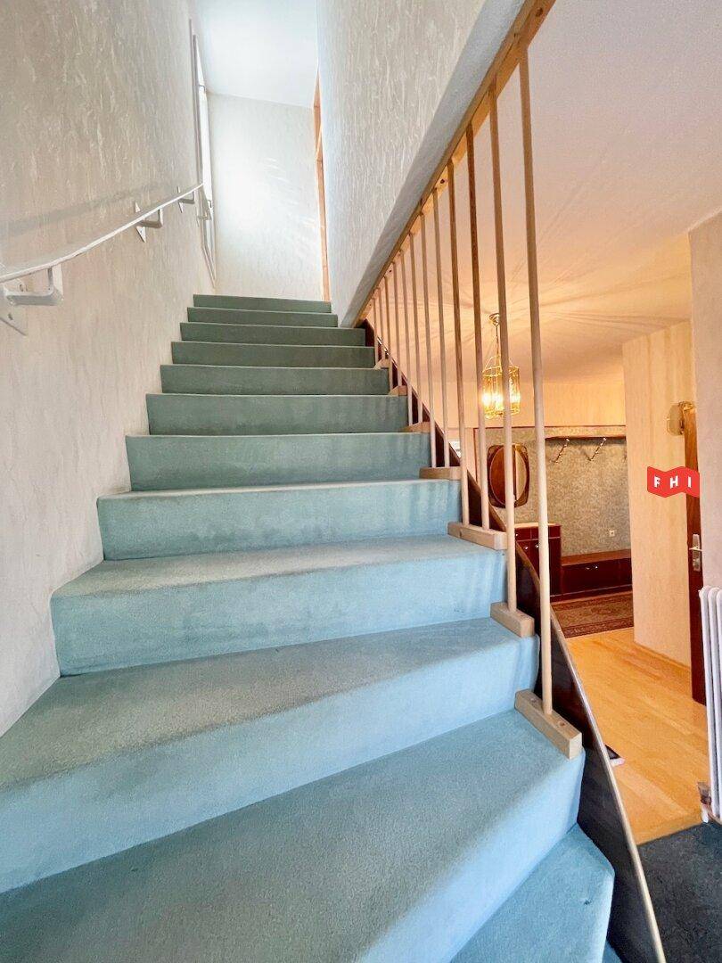 Treppenaufgang mit Teppichboden und Holzgeländer, der die Etagen verbindet.