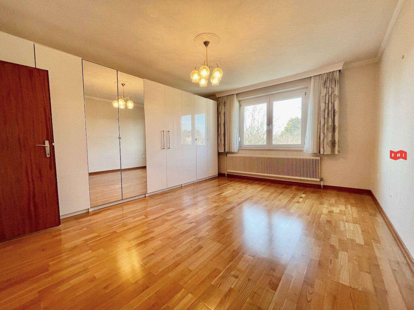Helles Schlafzimmer mit Parkettboden, Spiegelschränken und Blick ins Grüne.