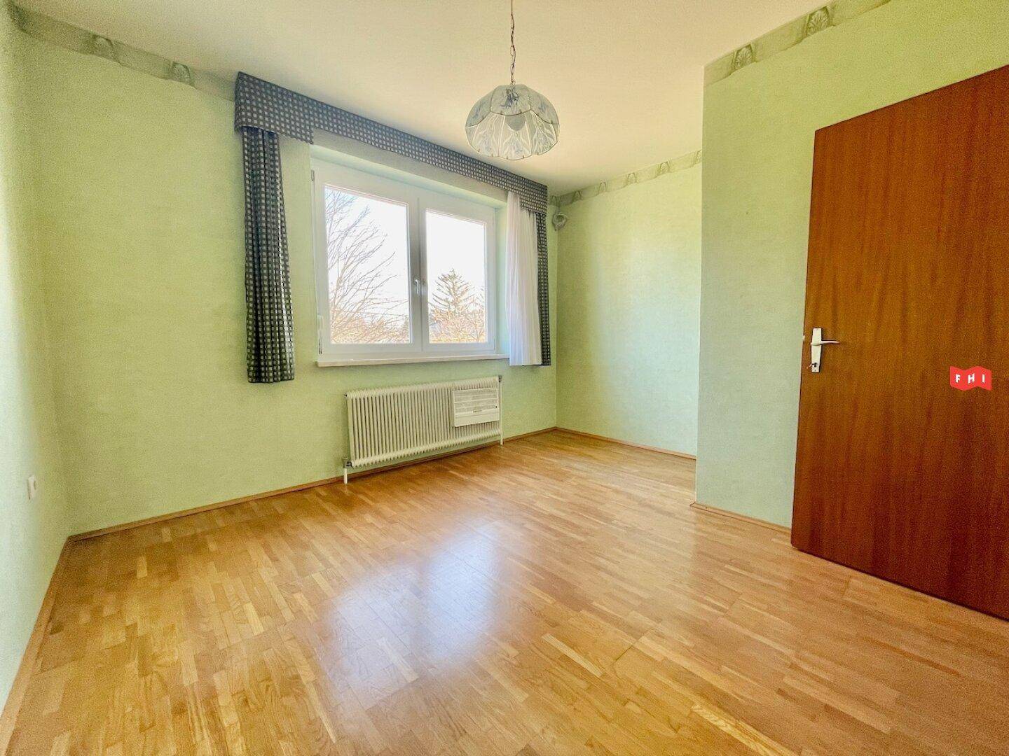 Helles Zimmer mit grün gestrichenen Wänden, Parkettboden und Fenster mit Ausblick.