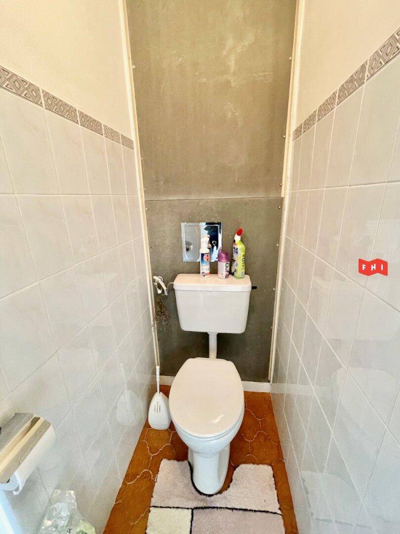 Separate Toilette mit weiß gefliesten Wänden und einem Fenster für Belüftung.