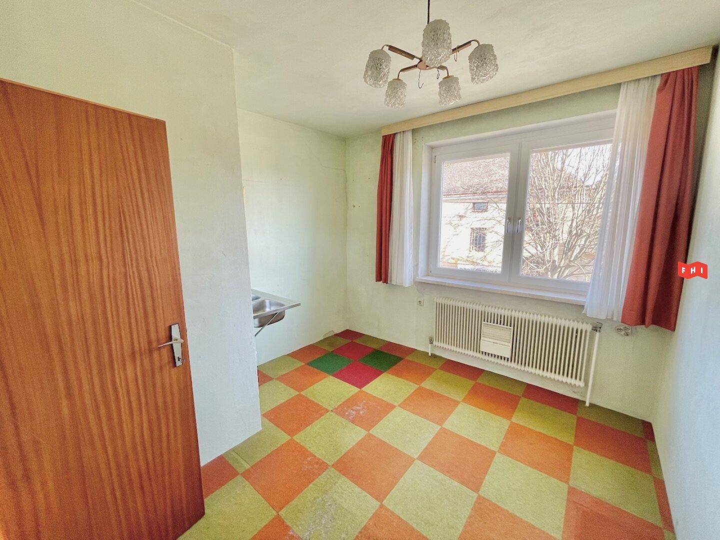 Kleiner Raum mit farbigem PVC-Boden, Fenster und einem Waschbecken.