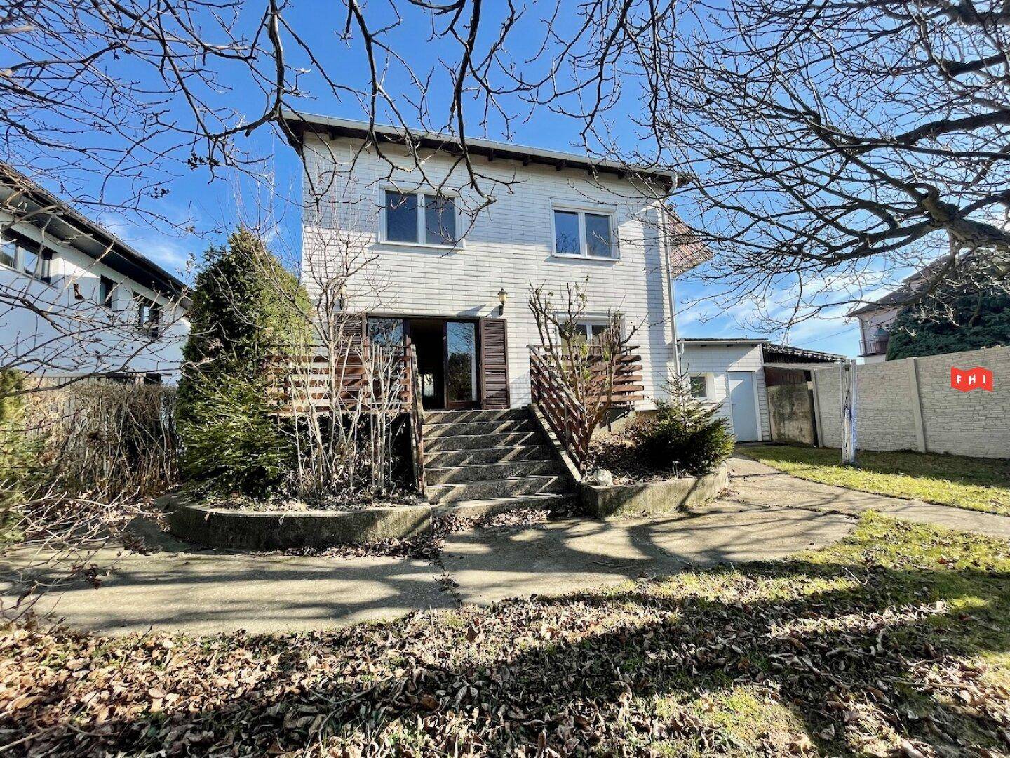 Rückansicht des Hauses mit Terrasse, Treppe zum Garten und angrenzender Garage.
