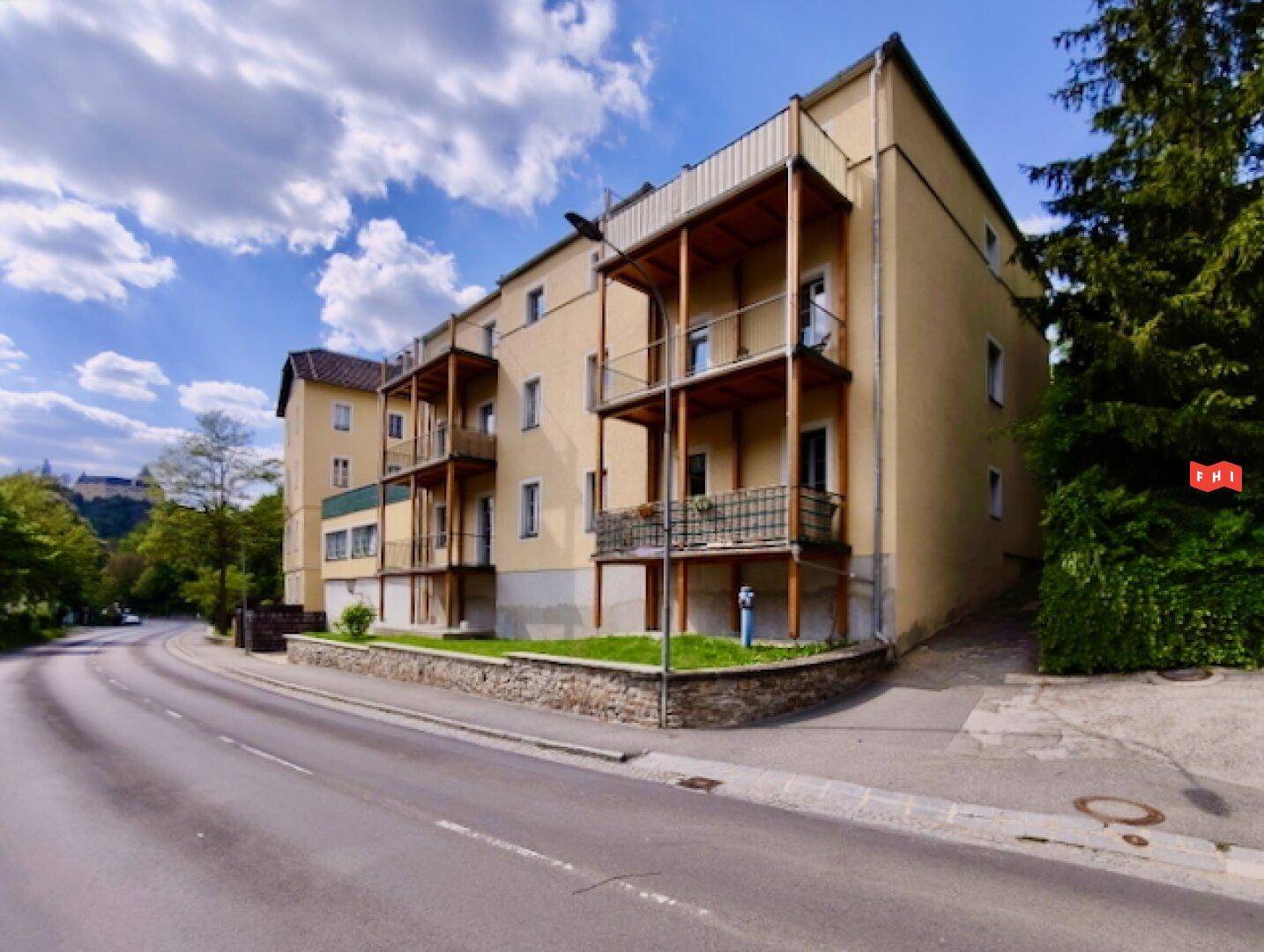 Gelbes Mehrfamilienhaus mit mehreren Balkonen und gepflegter Fassade an einer ruhigen Straße.