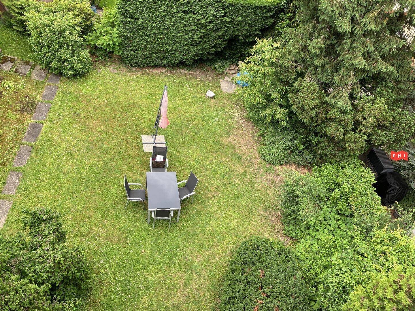 Gepflegter Gartenbereich mit Rasenfläche und einer möblierten Sitzgruppe unter einem Sonnenschirm.