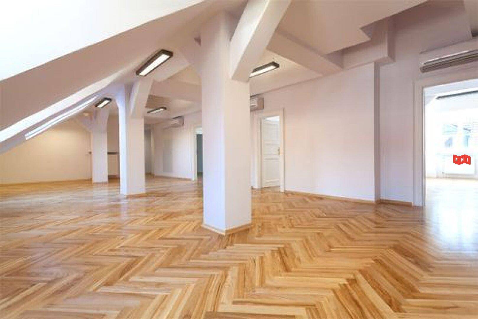Geräumiger, leerer Raum mit Fischgrätparkett, tragenden Säulen und Dachschrägen.
