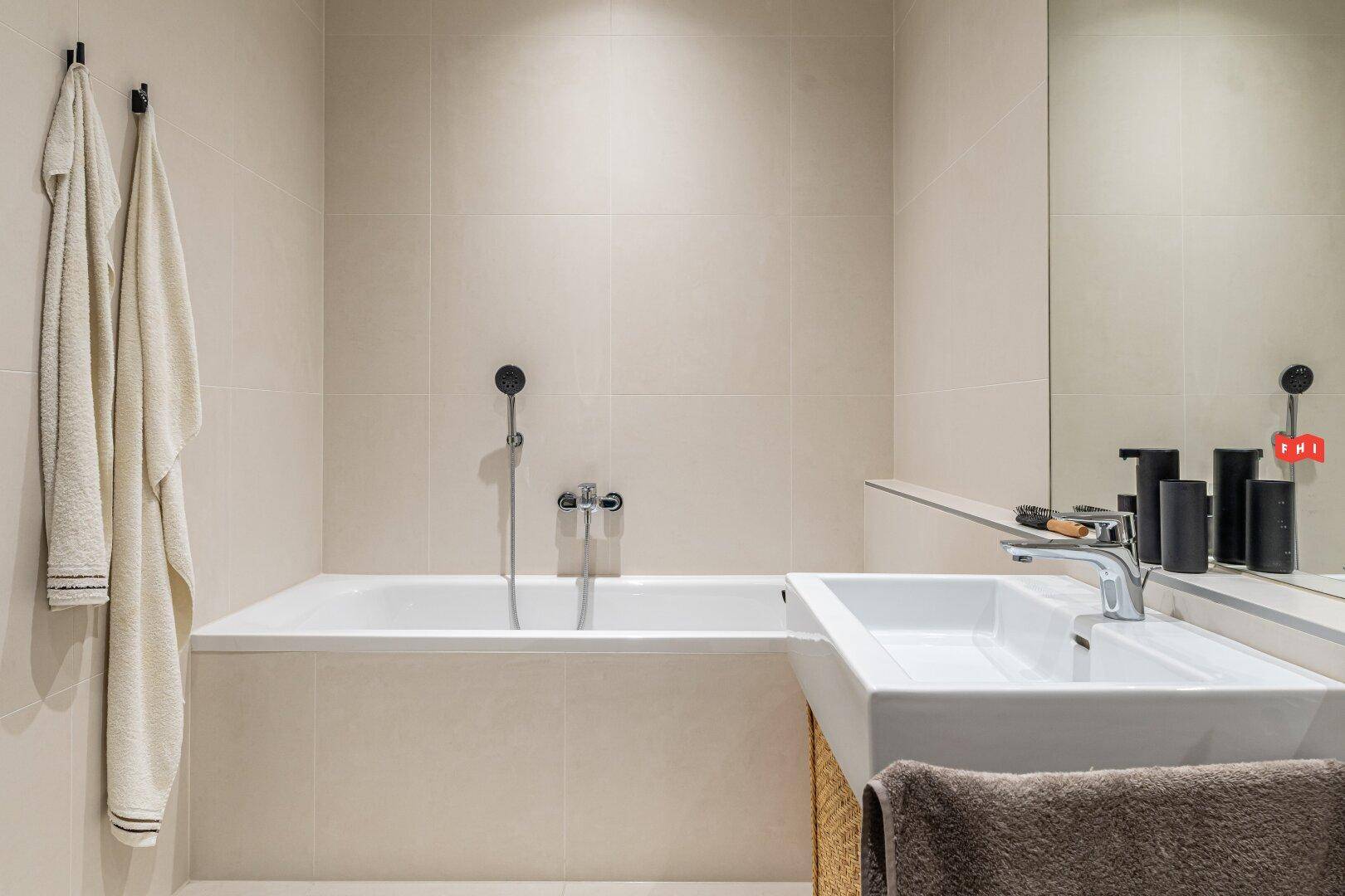Modernes Badezimmer mit Badewanne, Einzelwaschbecken und hellen Fliesen an Wänden und Boden.