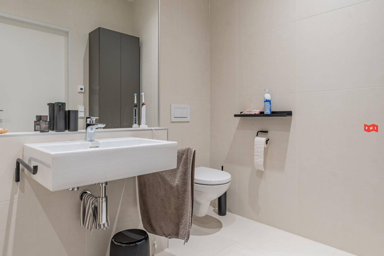 Gäste-WC mit wandhängender Toilette, Einzelwaschbecken und hellen, modernen Fliesen.