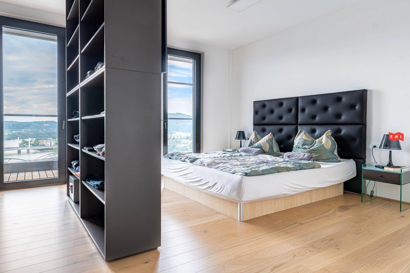Helles Schlafzimmer mit großem Bett, integriertem Regal und Panoramafenstern mit Stadtblick.