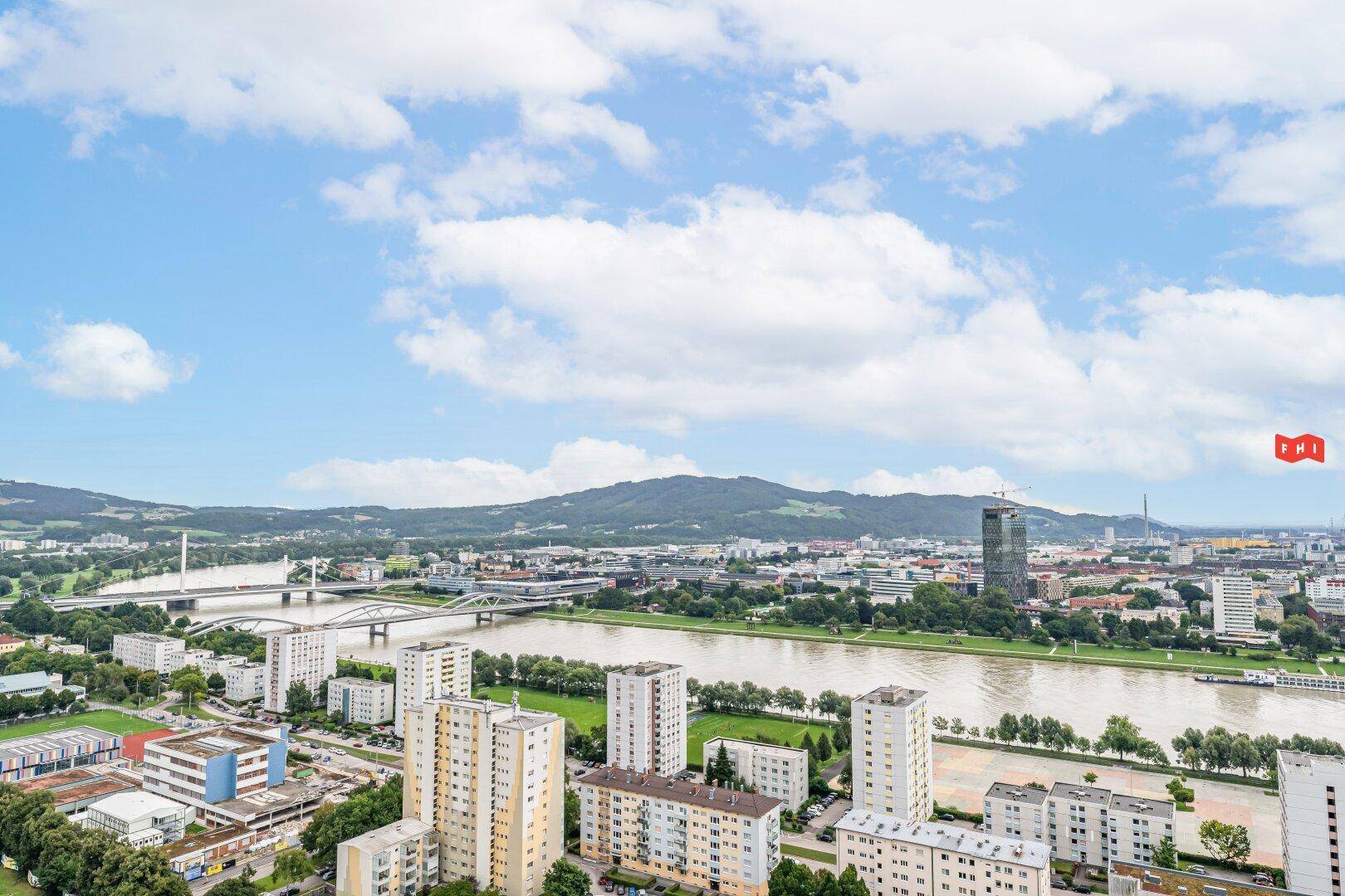 Panoramablick über die Stadt, den Fluss und die umliegende Berglandschaft unter blauem Himmel.