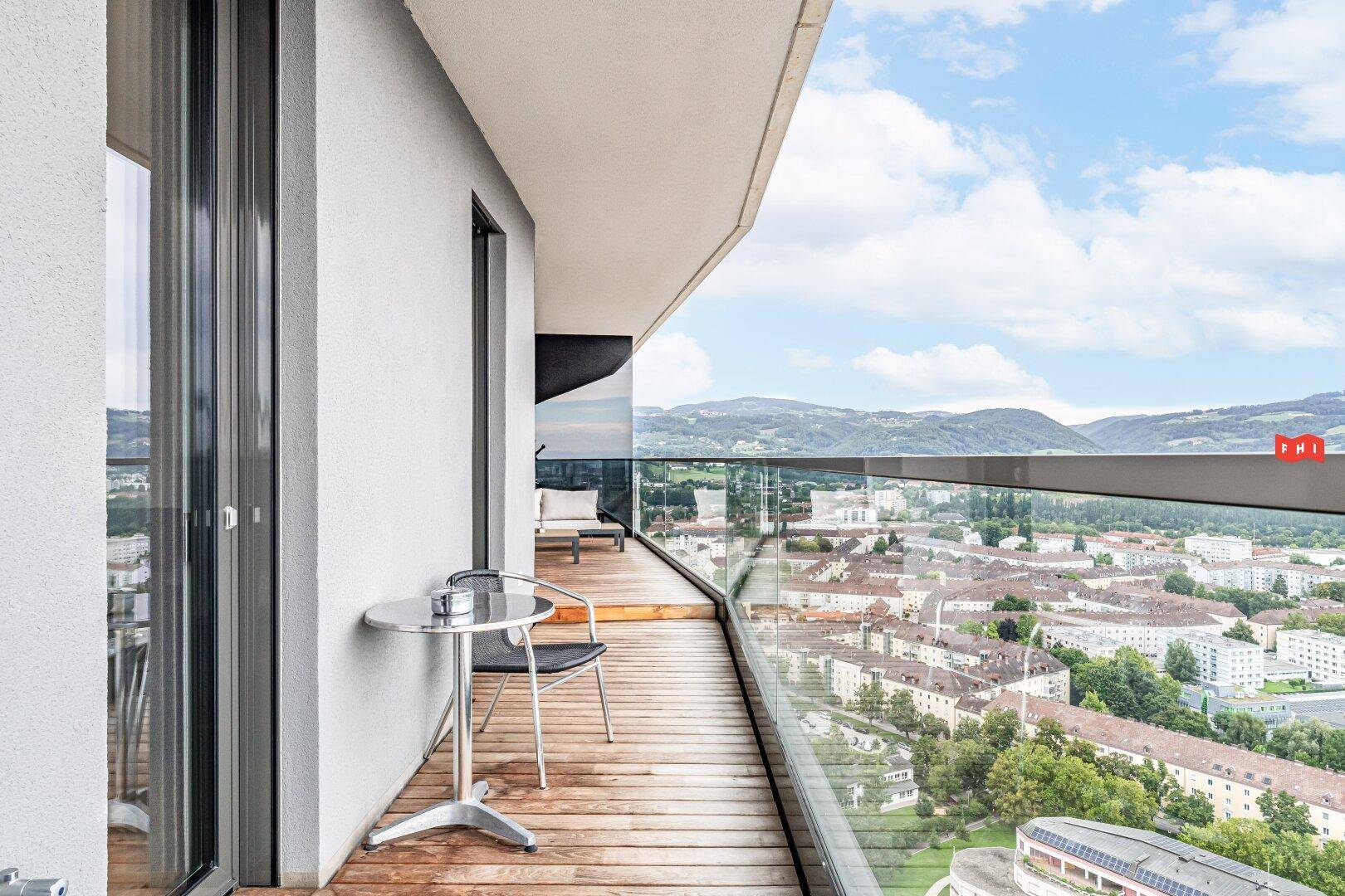 Schmaler Balkon mit kleinem Tisch und Stuhl, bietet einen weiten Blick über die Stadt.