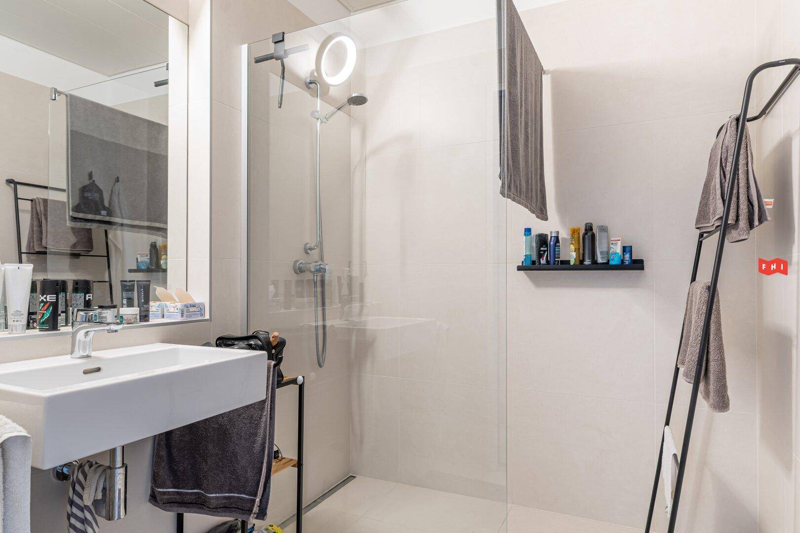 Modernes Badezimmer mit begehbarer Dusche, Einzelwaschbecken und hellen Fliesen.