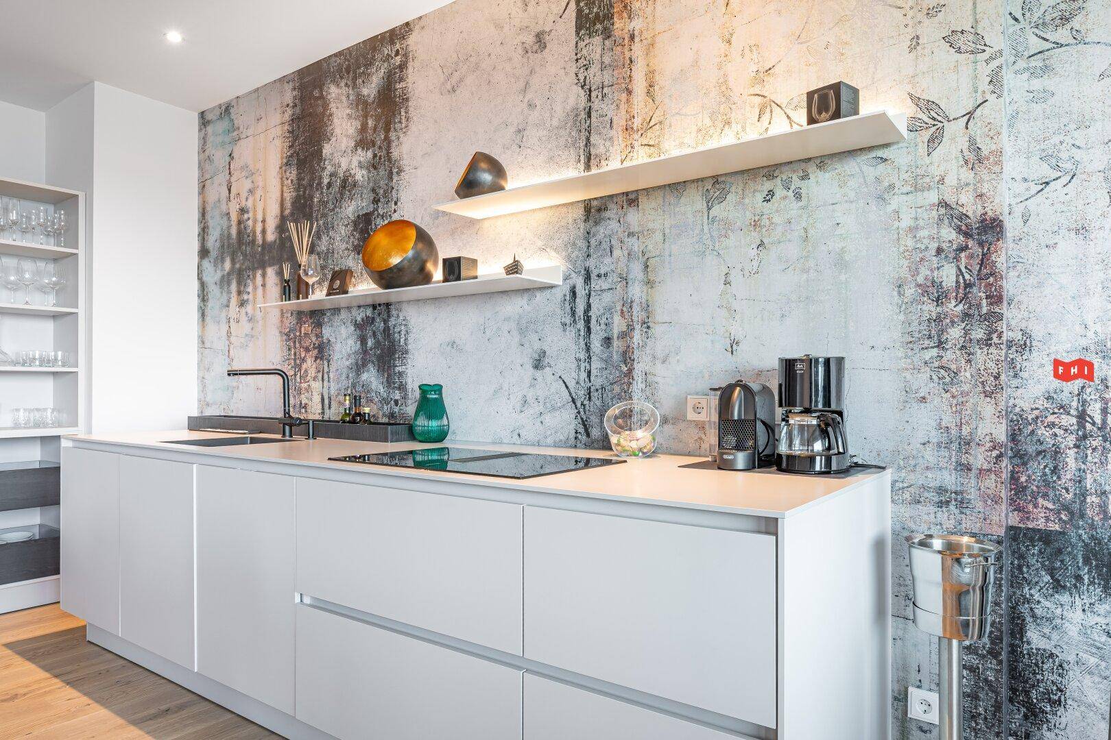 Moderne Einbauküche mit Induktionskochfeld, Kaffeemaschine und stilvoller Wandgestaltung.