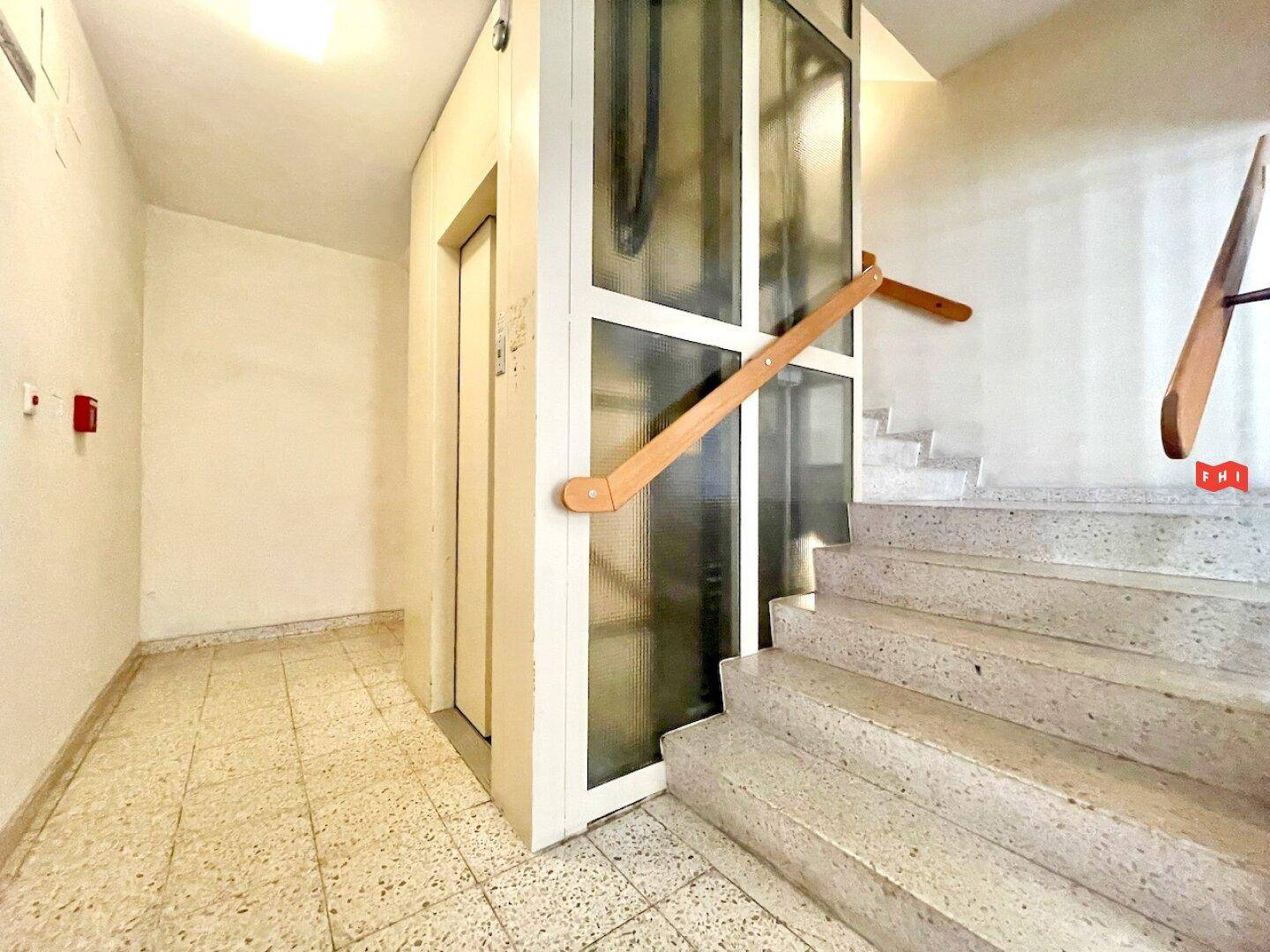Heller Eingangsbereich mit Treppe und modernem Aufzug, gut zugänglich.