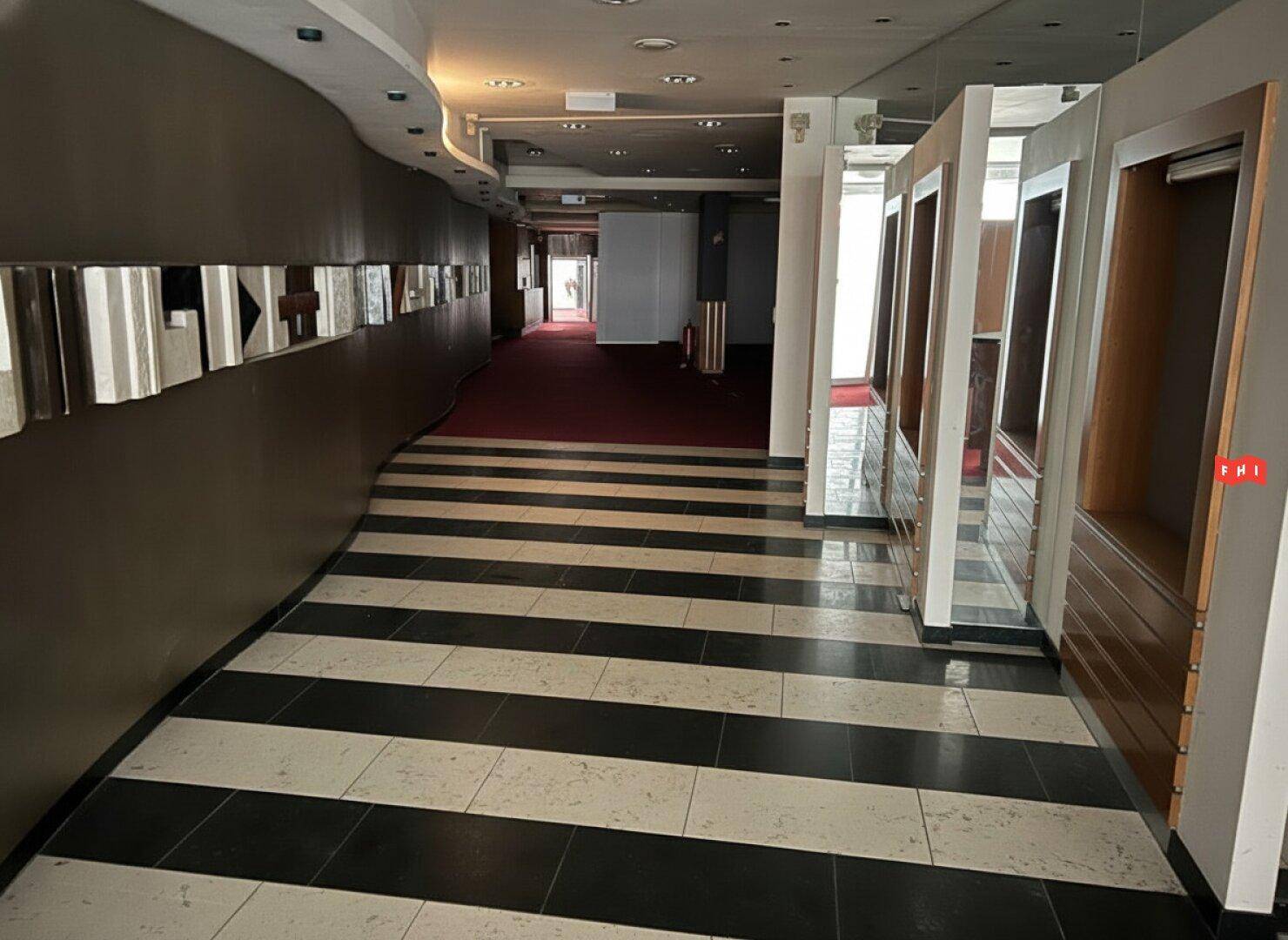 Langer Flur mit auffälligem schwarz-weiß gestreiftem Boden und roten Teppichböden im Hintergrund.