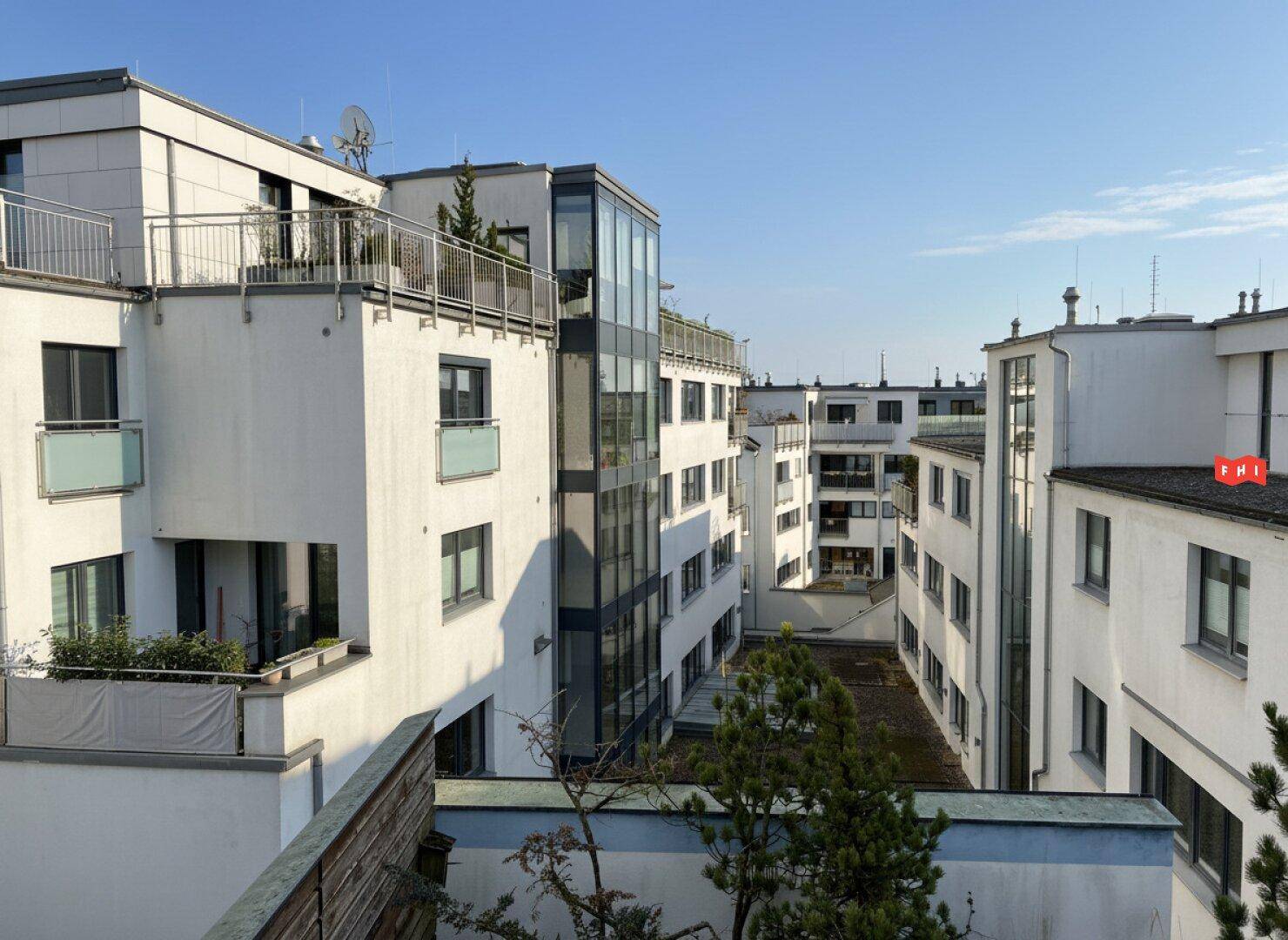 Innenhof eines modernen Wohnkomplexes mit weißen Fassaden, Balkonen und viel Grün.
