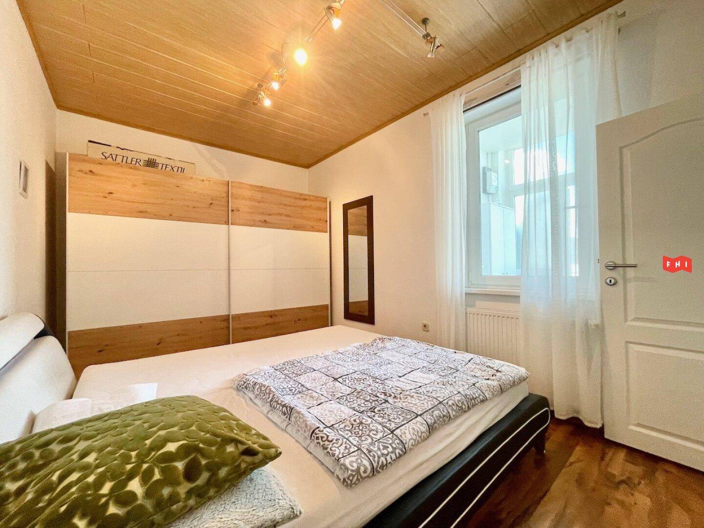 Schlafzimmer mit Holzdecke, großem Kleiderschrank und Fenster mit Vorhängen.