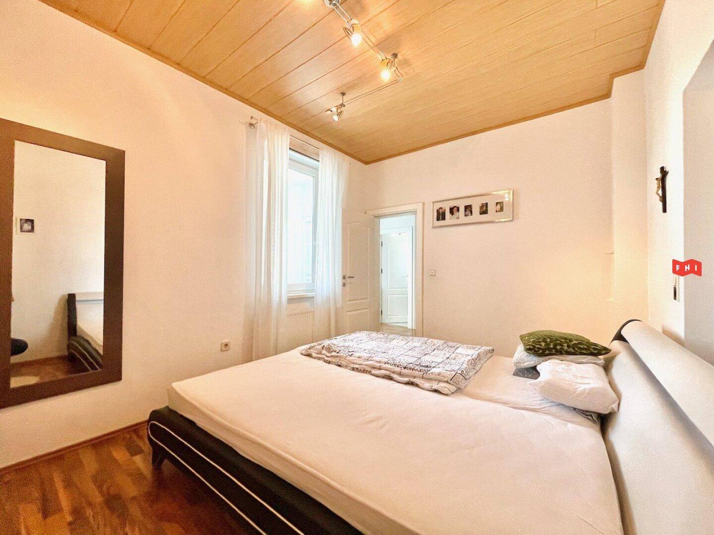 Helles Schlafzimmer mit Holzdecke, Doppelbett und großem Spiegel.