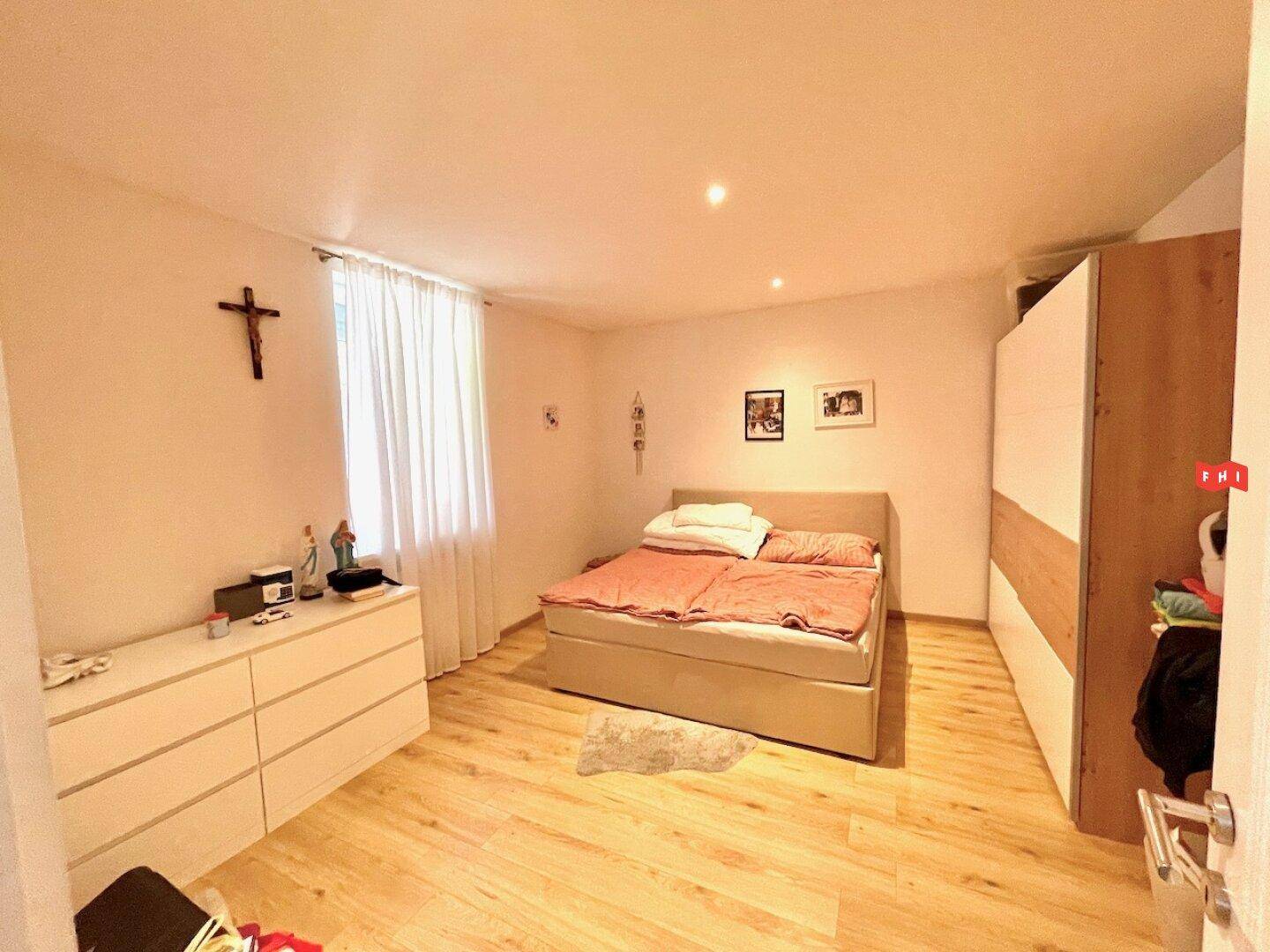 Schlafzimmer mit hellem Holzboden, großem Bett und weißer Kommode.