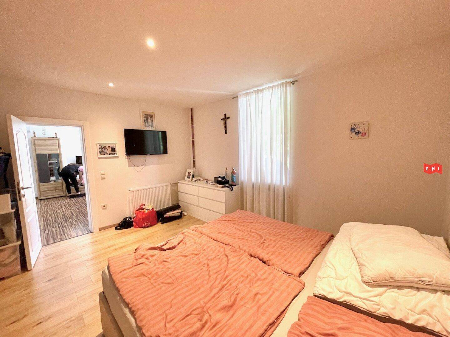 Geräumiges Schlafzimmer mit hellem Holzboden, Doppelbett und Blick auf den Flur.