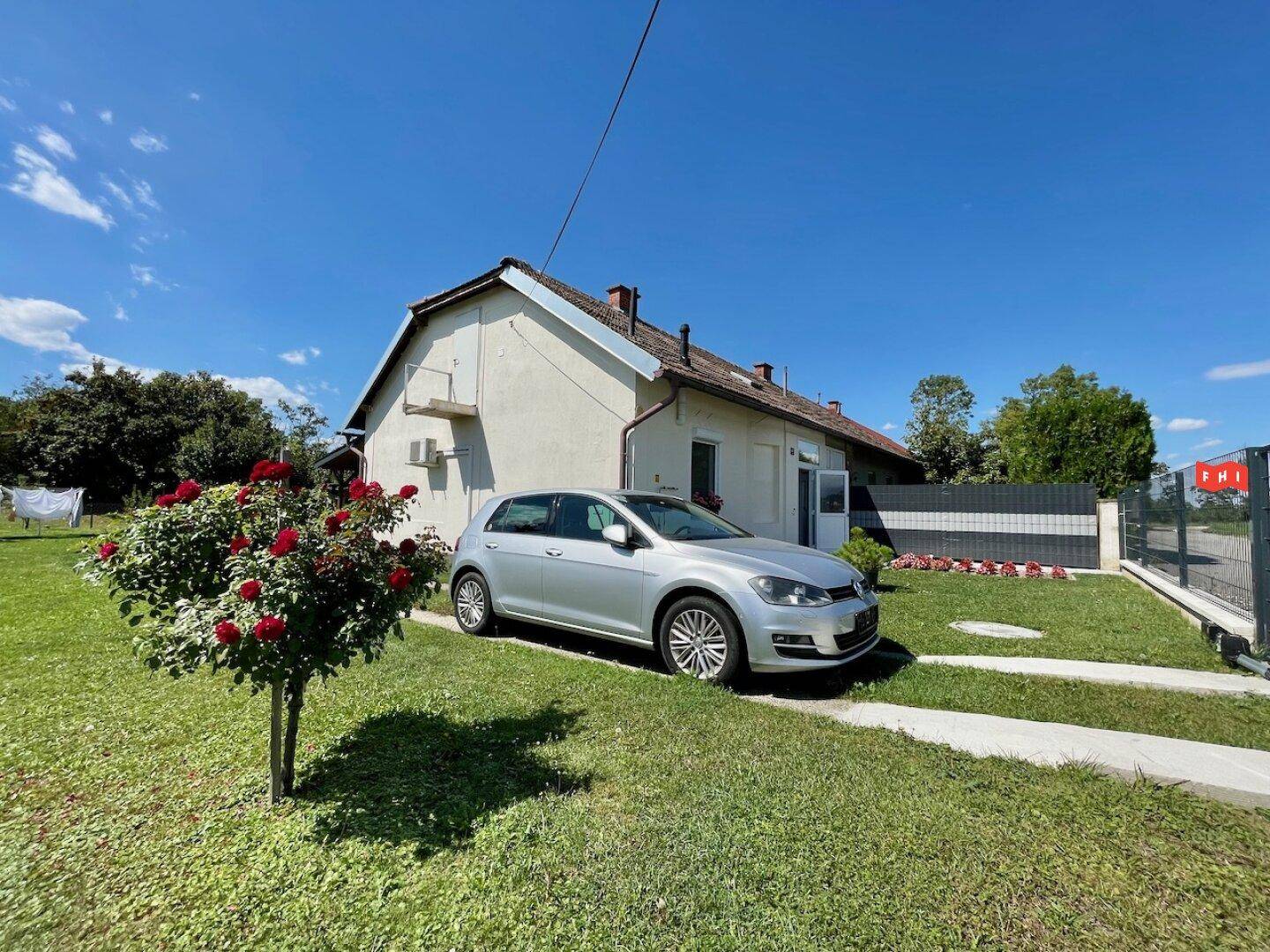 Vorderer Gartenbereich mit geparktem Auto, Rosenbusch und Blick auf das Wohnhaus.