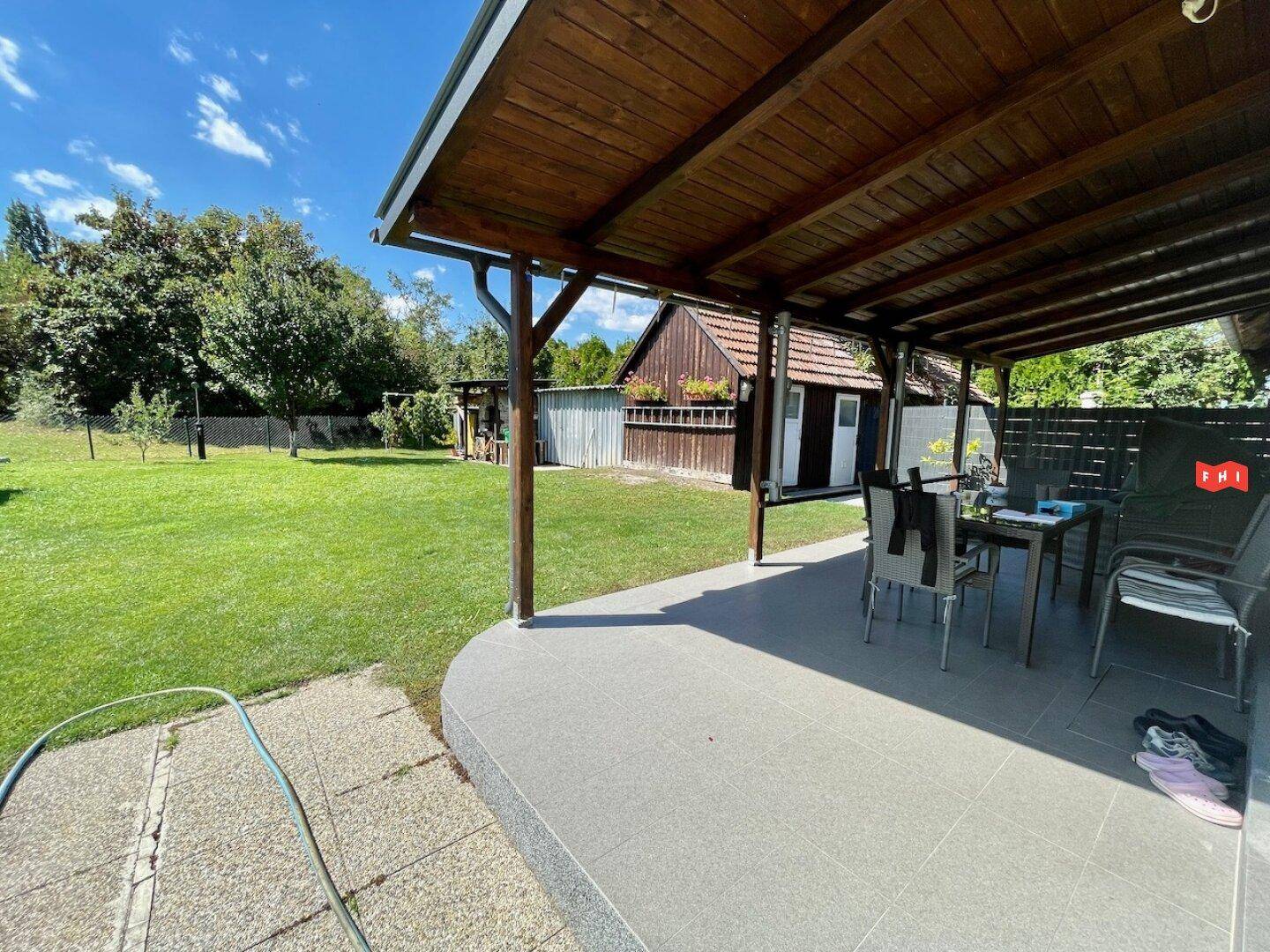 Überdachte Terrasse mit Fliesenboden und Gartenmöbeln, ideal für Mahlzeiten im Freien.